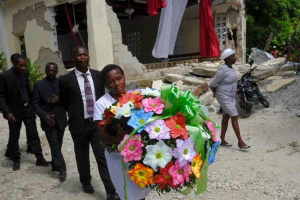 Des gens apportent une offrande de fleurs à côté de l’église détruite par le tremblement de terre où le ministre de l’Église baptiste Andre Tessono est mort, lors de ses funérailles dans le quartier de Picot aux Cayes, Haïti, dimanche 22 août 2021, huit jours après qu’un tremblement de terre de magnitude 7,2 a frappé la région.