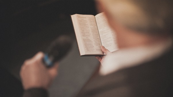 Man preaching into a microphone and holding a Bible